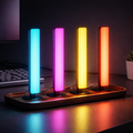 Four RGB light bars on walnut tray beside monitor — ambient desk lighting and room decor