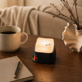 Small cube light on a wooden table with a cup of coffee, notebook, and pen in a cozy setting.